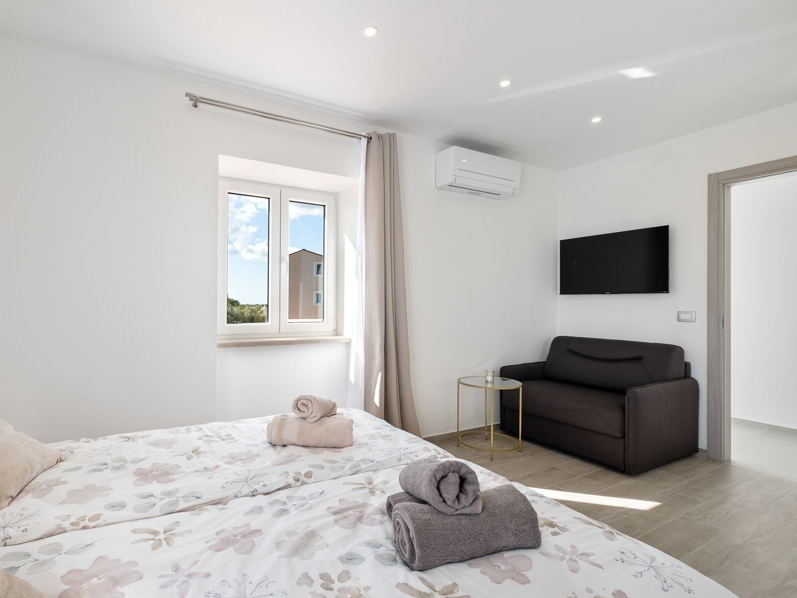Une chambre moderne avec un lit, une télévision, un canapé et une fenêtre avec des rideaux.