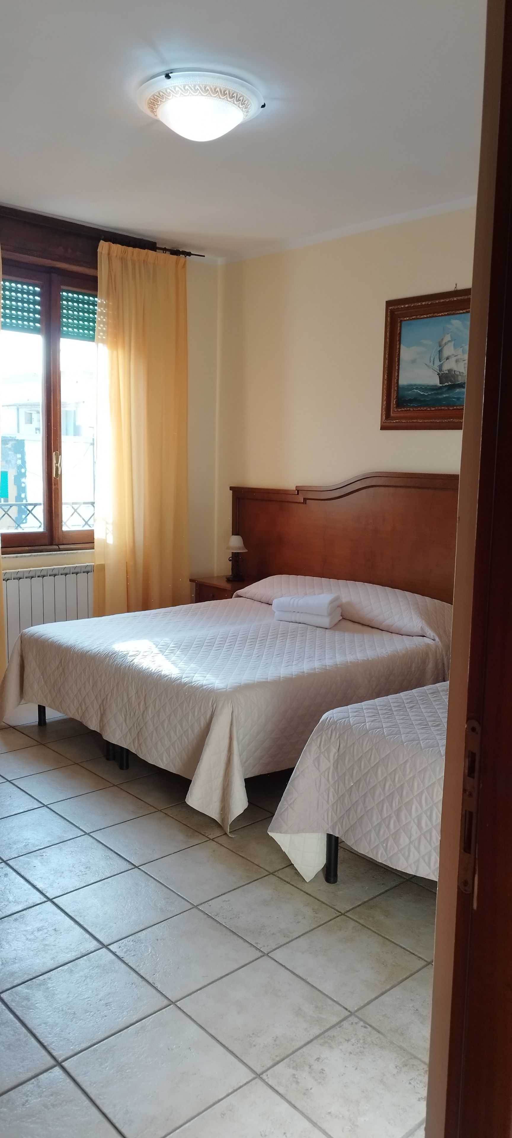 Un dormitorio con una cama doble, una mesita de noche, una lámpara y una ventana con cortinas.