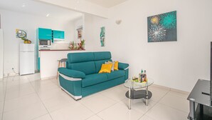 A modern living room with a teal sofa, a glass coffee table, and a kitchen area in the background. - Verbena at the Refuge de Madiana in Schoelcher 1036 eg-supply-onboarding-api eg-supply-onboarding-api (Schoelcher)