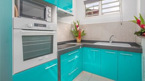 A kitchen with teal cabinets, a microwave, an oven, a sink, and a window with a view. - Verbena at the Refuge de Madiana in Schoelcher 1036 eg-supply-onboarding-api eg-supply-onboarding-api (Schoelcher)