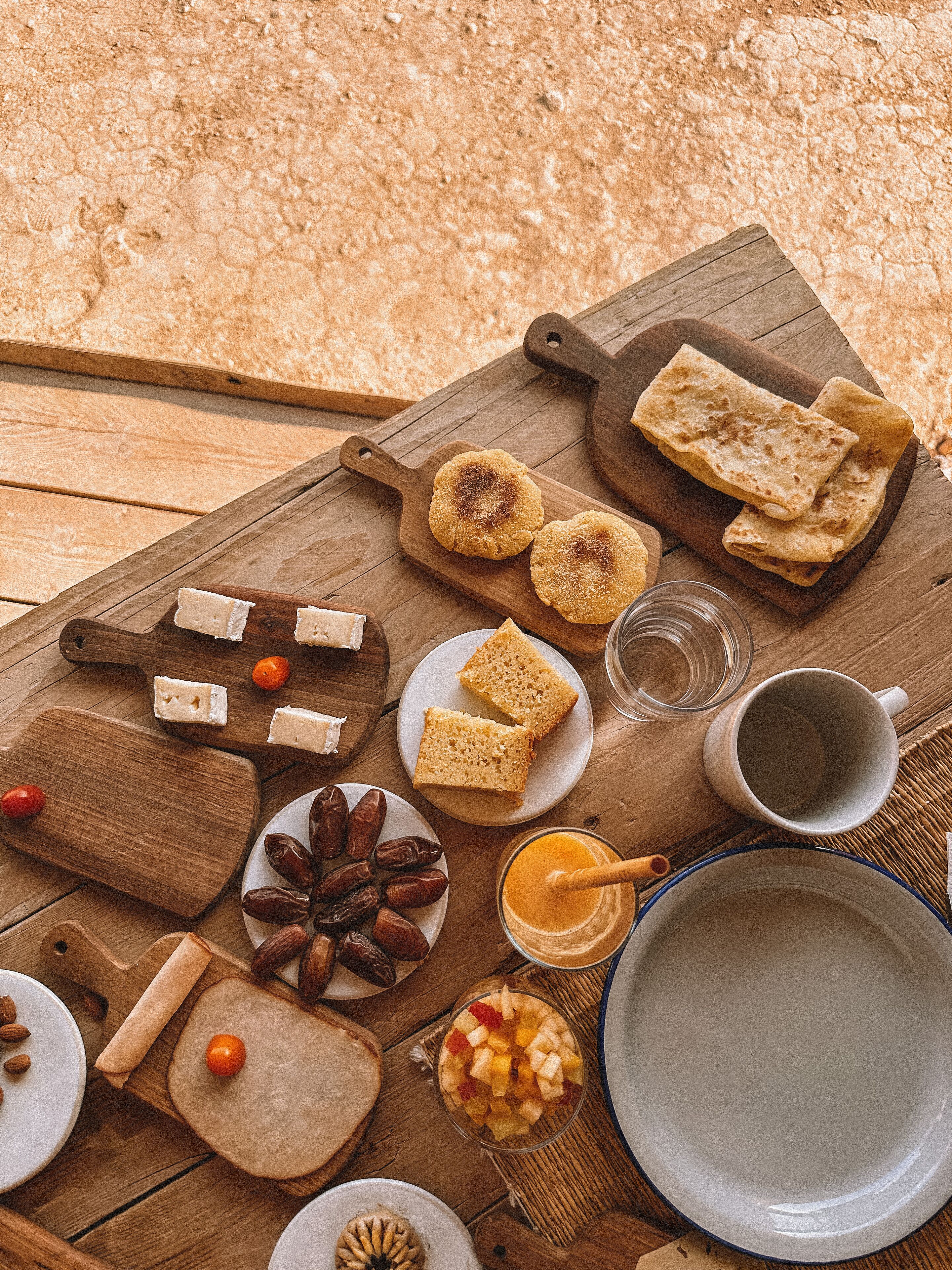 Ein Holztisch mit verschiedenen Speisen, darunter Brot, Käse, Datteln und einer Schüssel Obst.