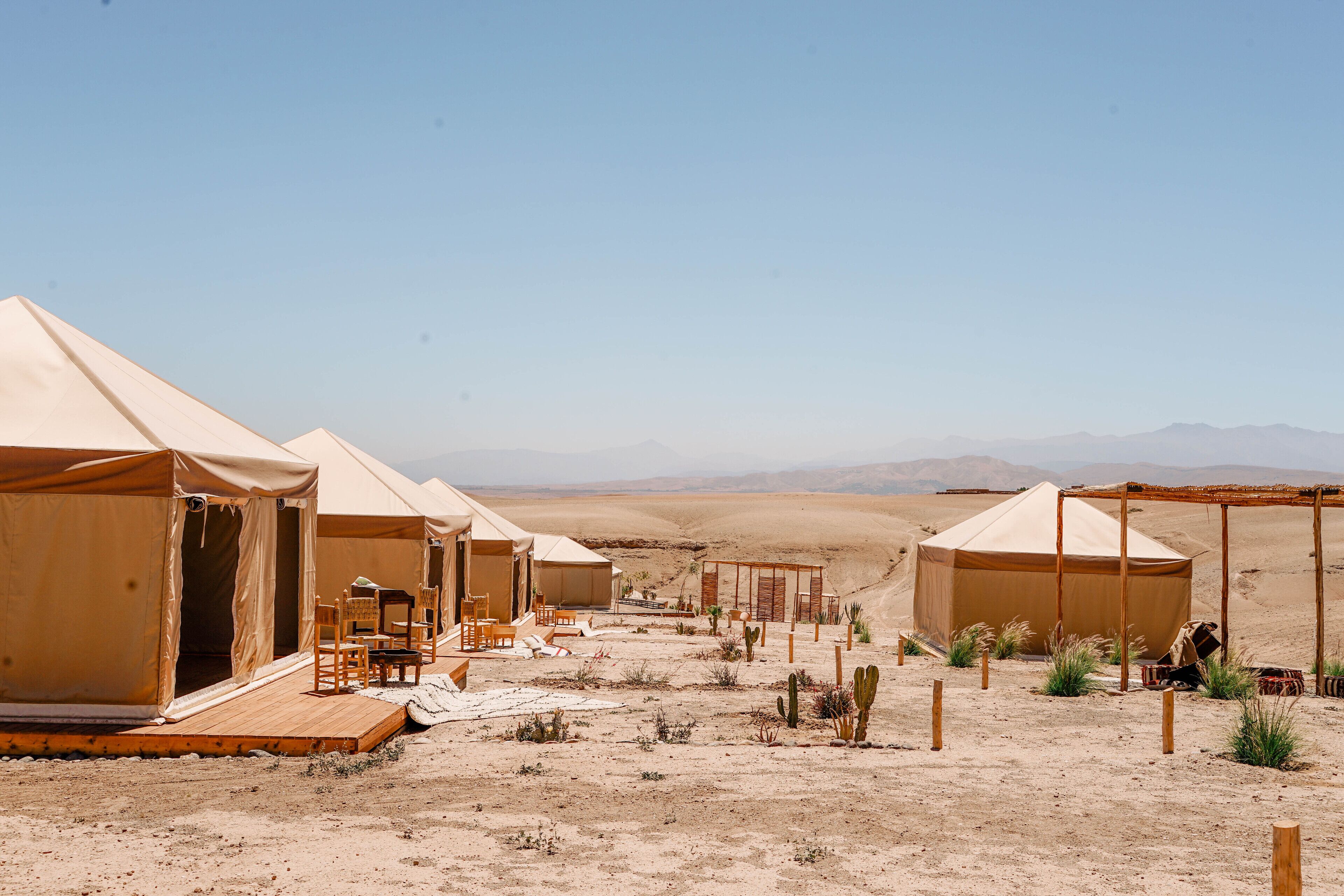 Un campamento en el desierto con varias tiendas de campaña, muebles de madera y vegetación escasa.
