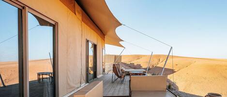 A desert-view balcony with a wooden deck, cushioned seating, and a round wooden table.