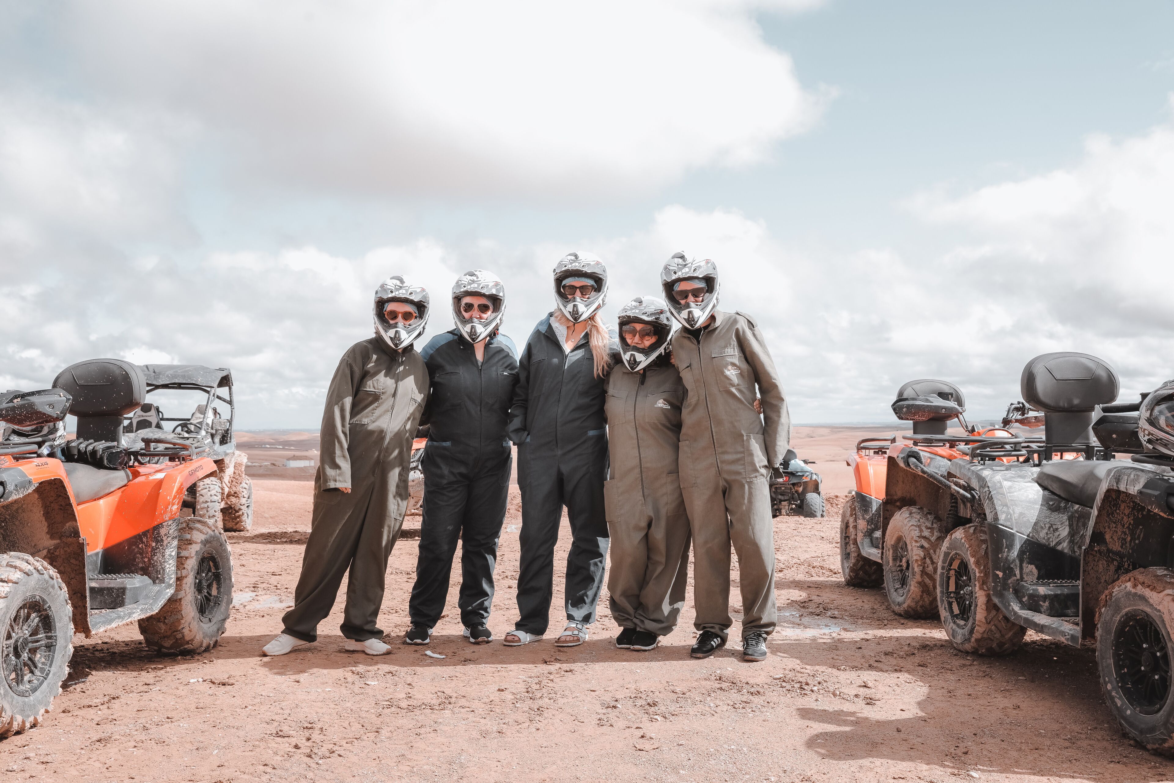 A group of people standing in a desert with ATVs in the background.