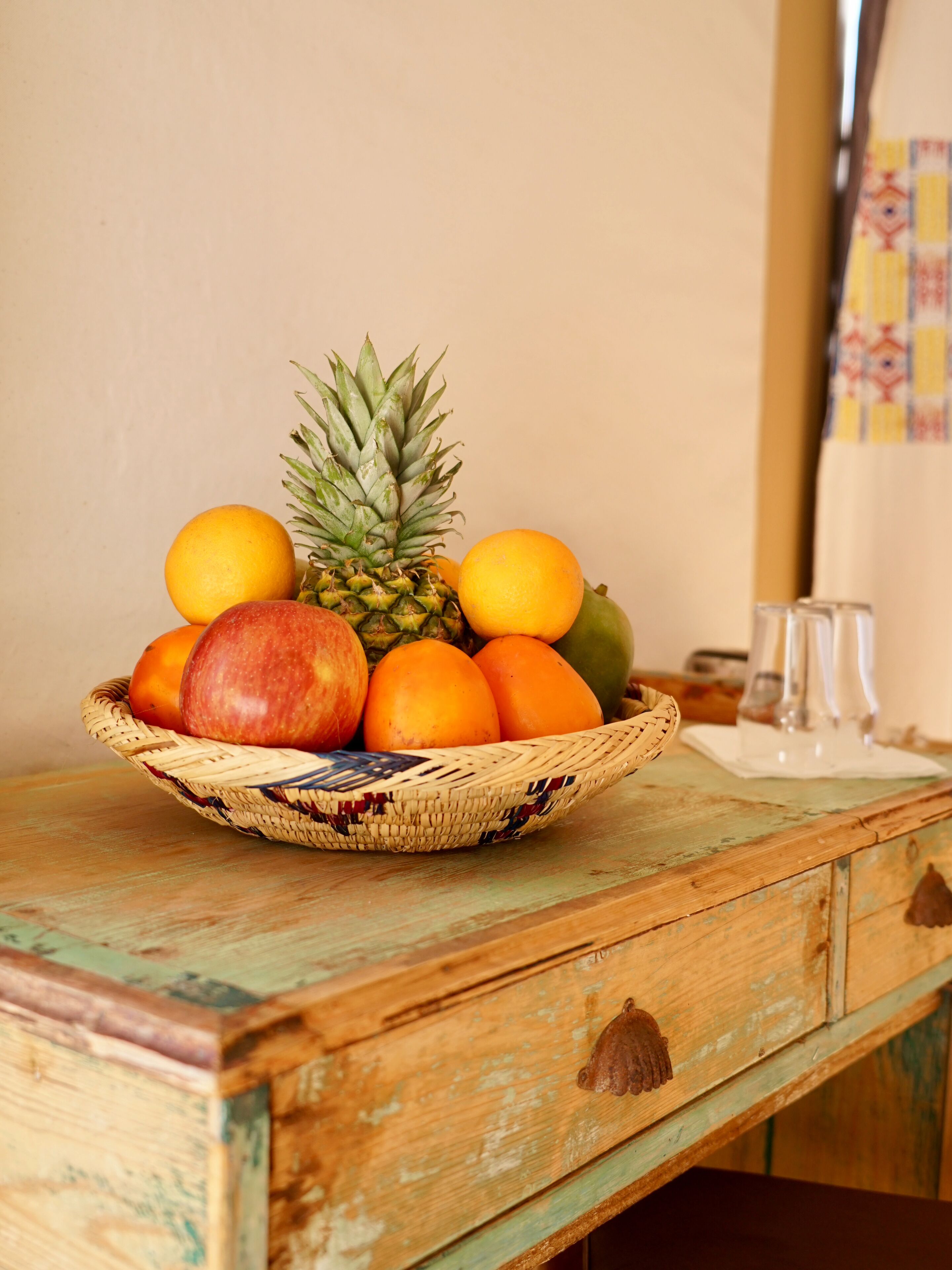 Une table en bois sur laquelle se trouve un panier tressé contenant des fruits et un verre.