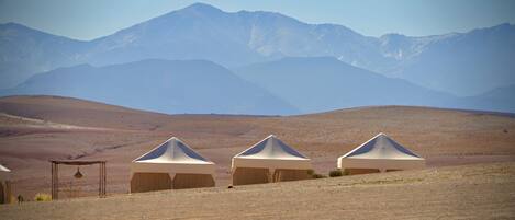 Three tents in a desert landscape with mountains in the background.