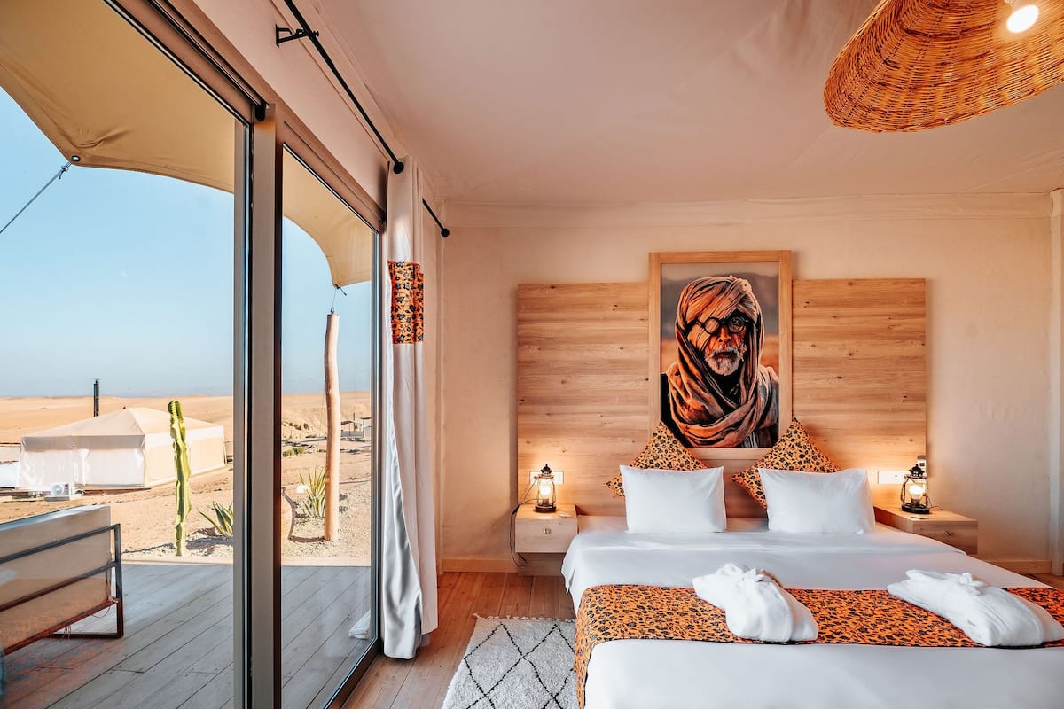 Un dormitorio con una cama grande, dos mesitas de noche, un cuadro en la pared y vistas al desierto a través de amplias ventanas.