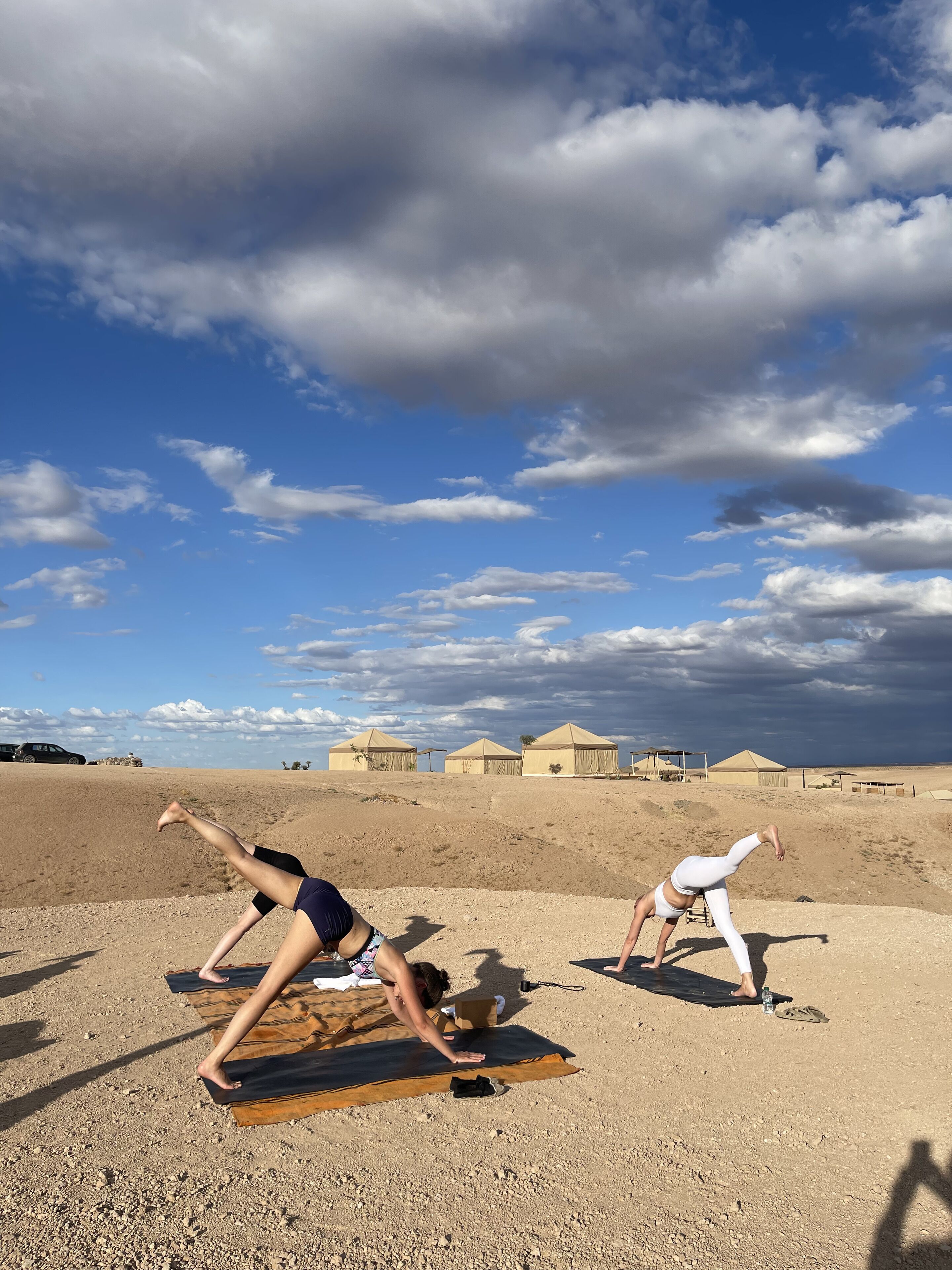 Two individuals practicing yoga on mats in an open area with tents in the background.