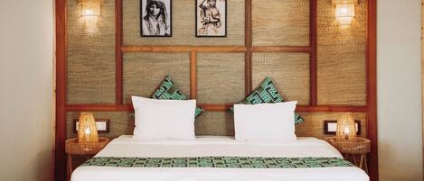 A neatly made bed with white linens, two pillows, and a green patterned bedspread. There are two wall-mounted lamps on either side of the bed.