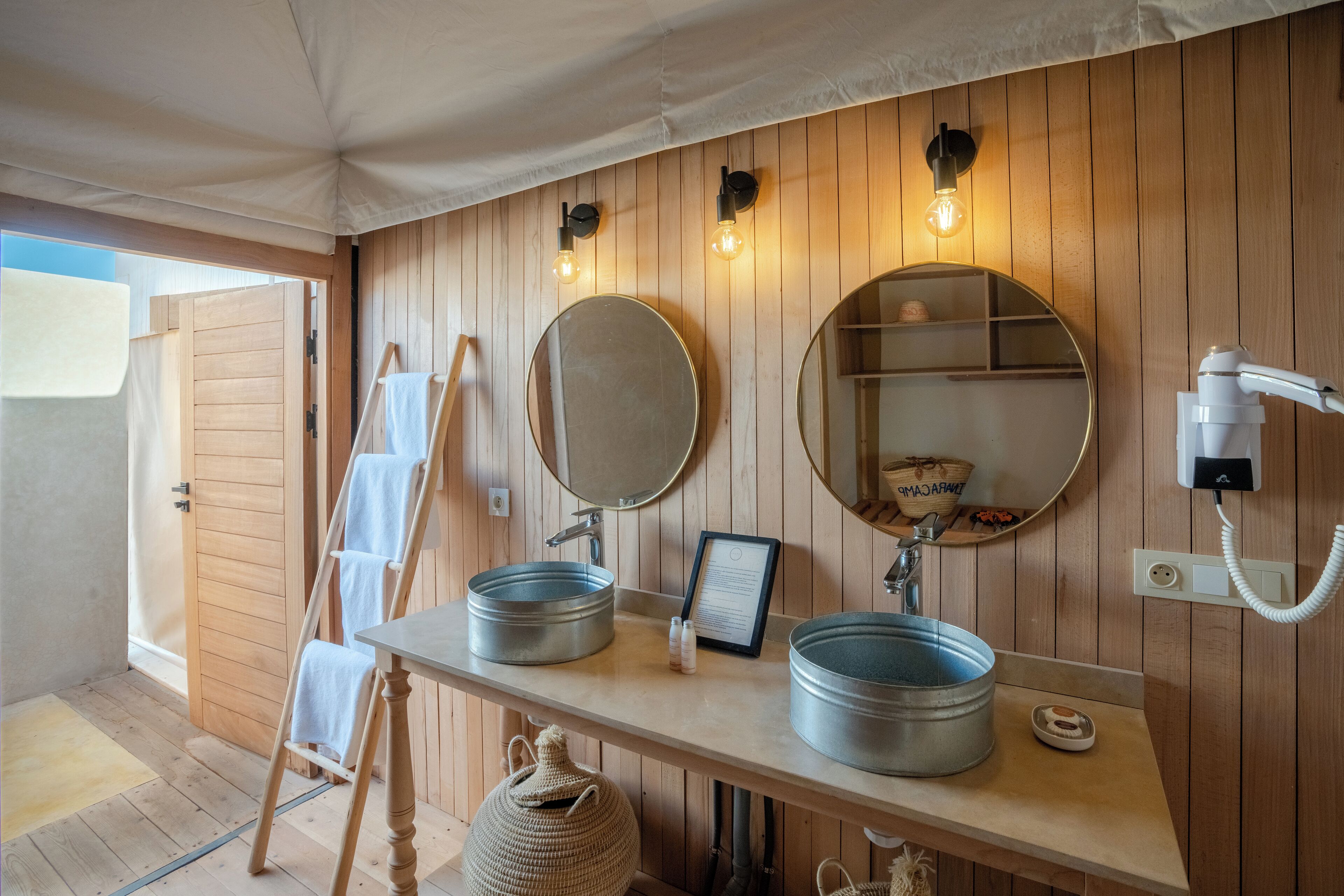 A wooden-paneled bathroom with two round mirrors, a sink, and a towel rack.
