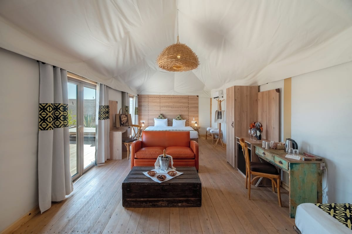 Una habitación amplia con una cama grande, un escritorio de madera, un sofá naranja cómodo y una mesa de comedor.