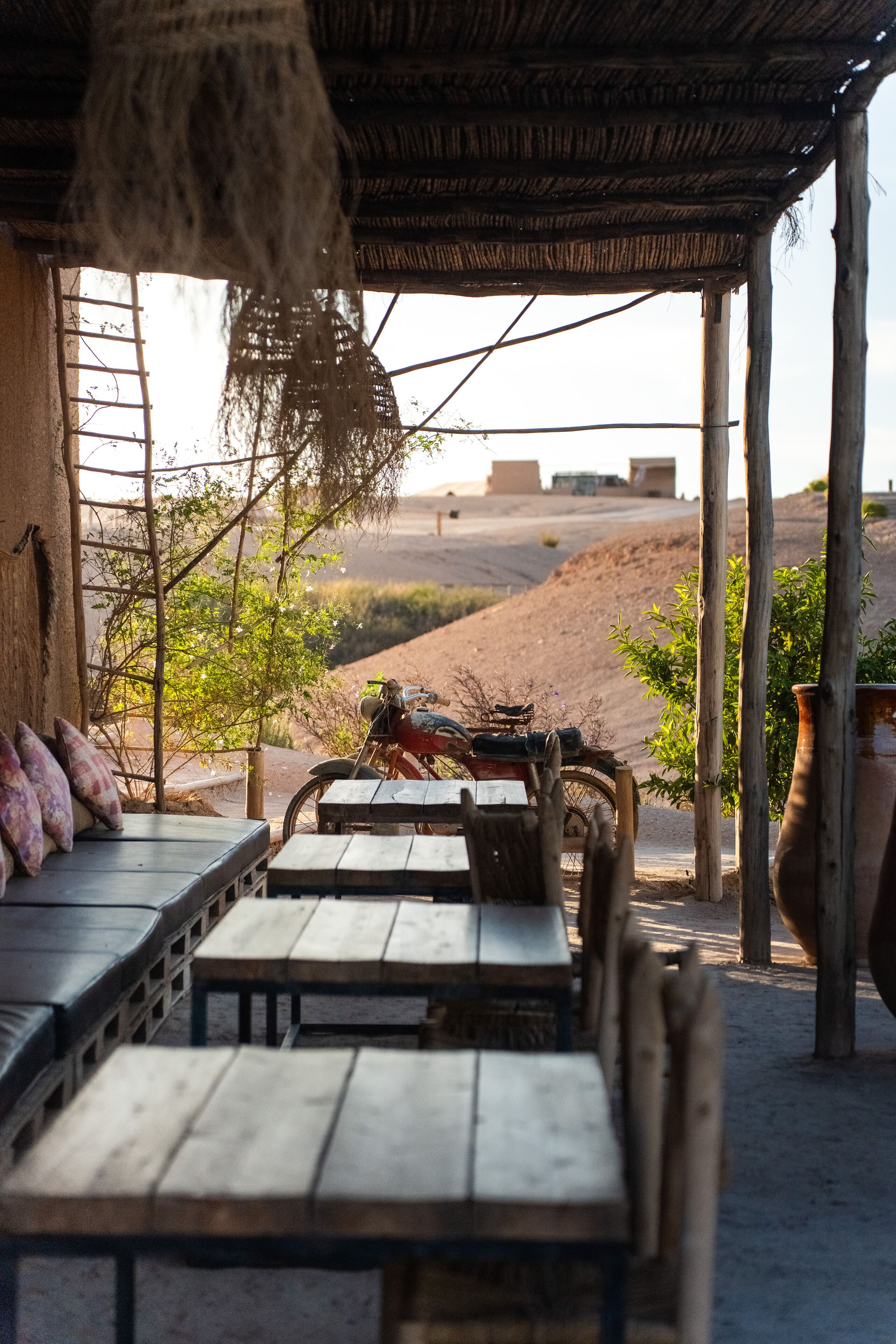 Un espacio al aire libre rústico con mesas y bancos de madera, techo de paja y vistas a un paisaje desértico.