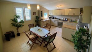 A compact kitchen with a dining table, chairs, and a microwave. There are potted plants and a bench near the window. - Captivating and Spacious 2-bed House in Vranovici (Ljesevici)