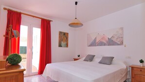 A bedroom with a bed, a nightstand, a dresser, a window with red curtains, and a painting on the wall.