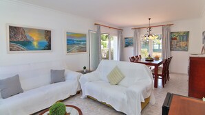 A living room with two white sofas, a dining table with chairs, and artwork on the walls.