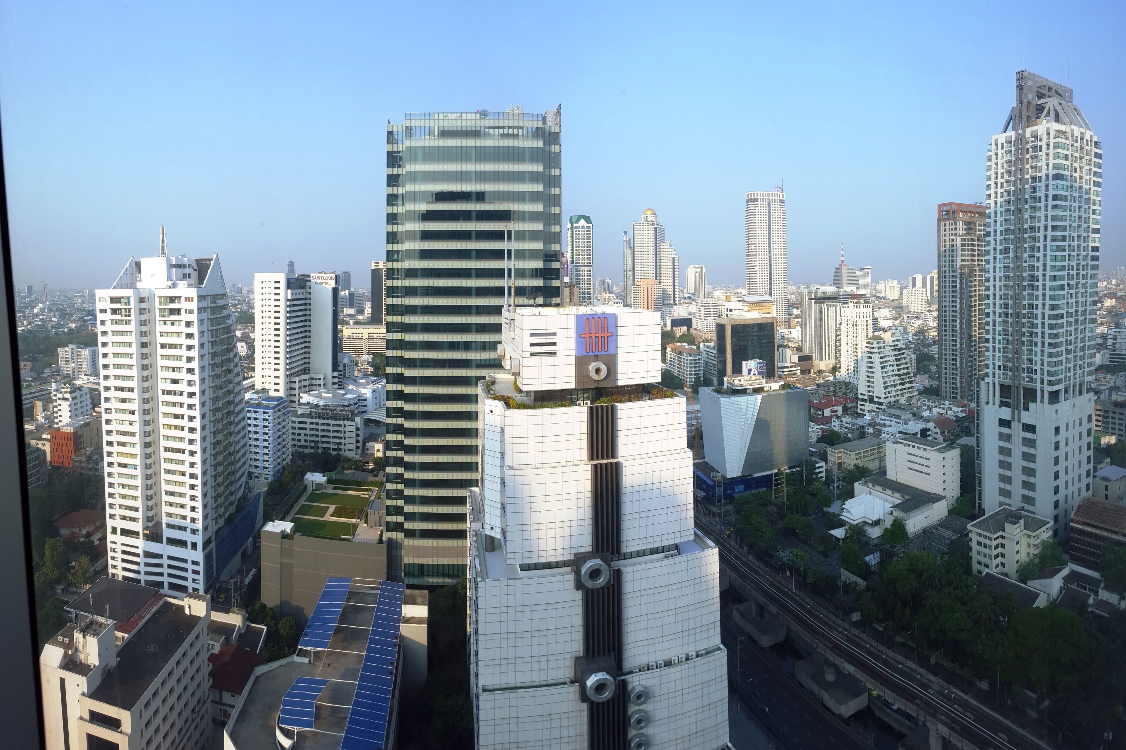 A cityscape with modern high-rise buildings, including a distinctive building with a unique architectural design featuring a grid-like facade and a rooftop garden.