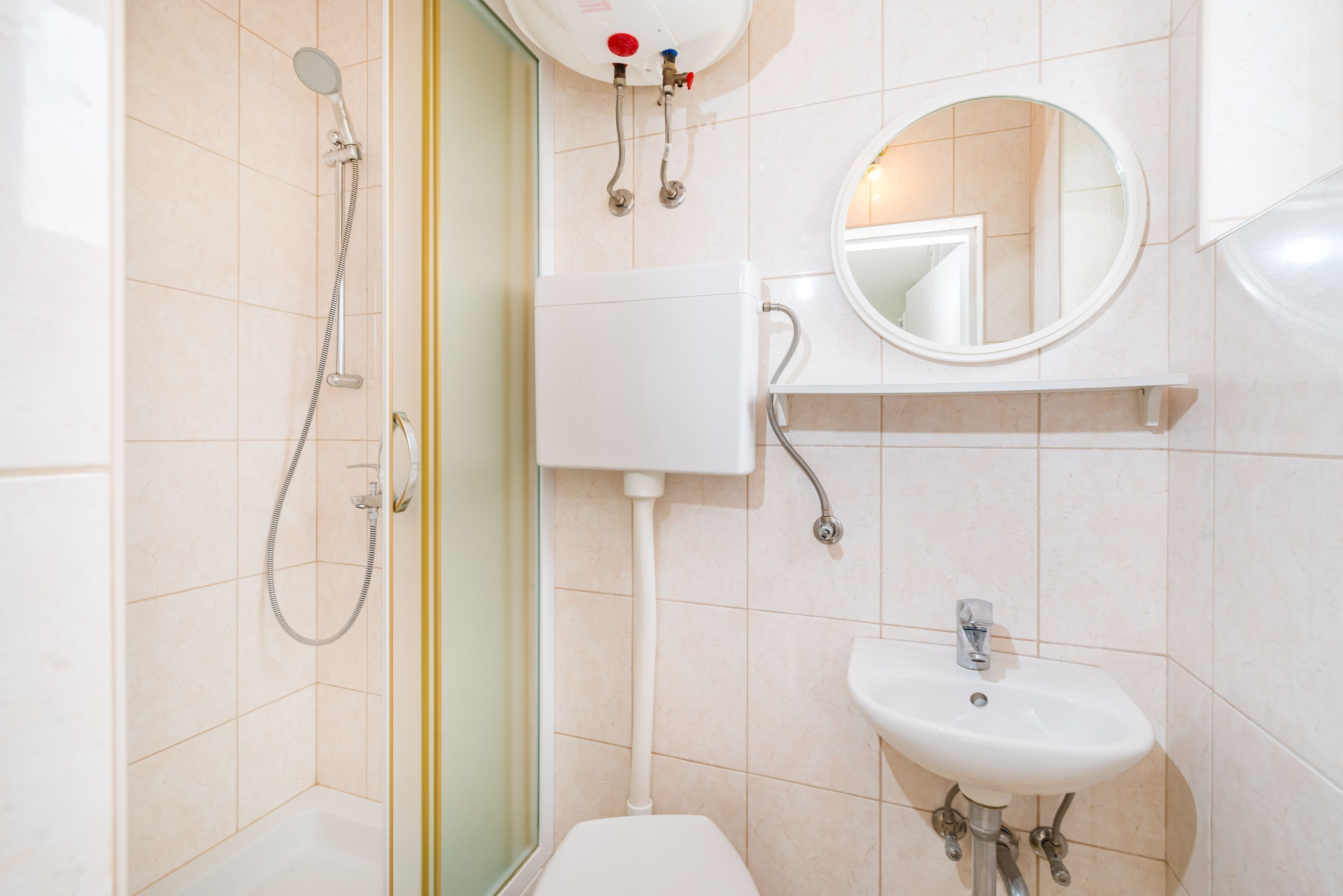 A bathroom with a toilet, a sink, a shower, and a mirror.