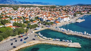 Luftaufnahme einer Küstenstadt mit einem Hafen, klarem, blauem Wasser und einem Bergpanorama.