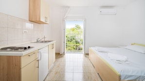 Ein kompaktes Zimmer mit einer Küchenzeile, einem Bett und einem Balkon mit Blick ins Grüne.