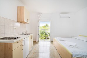Habitación compacta con kitchenette, cama y balcón con vista a la vegetación.