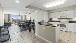 A modern kitchen with white cabinets, a central island, and a dining area with chairs and a table. - Yacht Club Villas #3-403 Spectacular Waterway View Condo! (North Myrtle Beach)