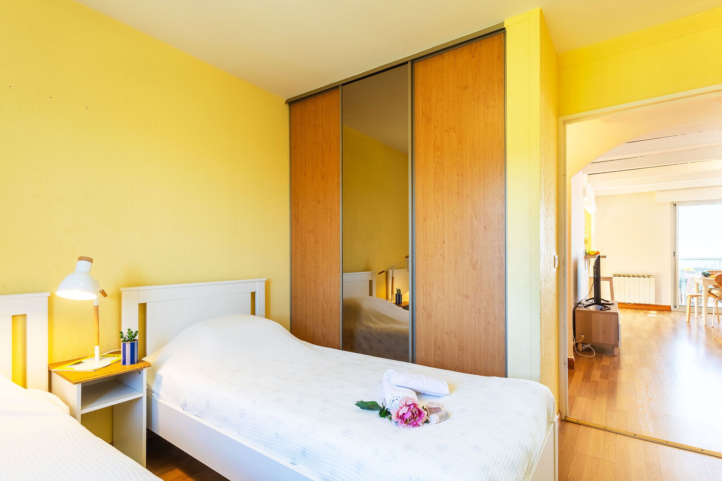 A hotel room with a bed, bedside table with a lamp, a mirror, and a wooden wardrobe.
