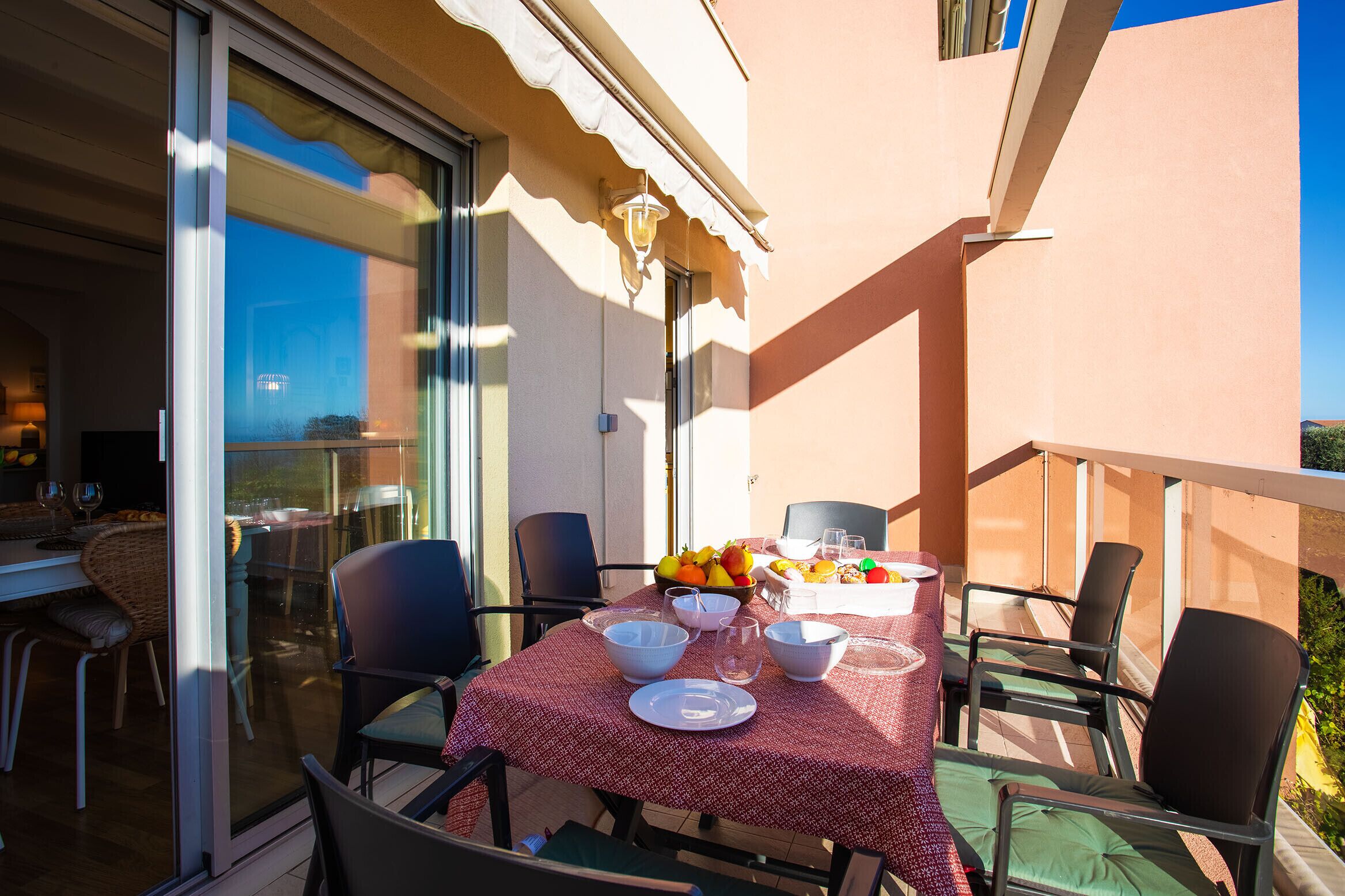 A balcony with a table set for dining, chairs, and a fruit bowl.