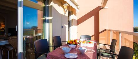 A balcony with a table set for dining, chairs, and a fruit bowl.