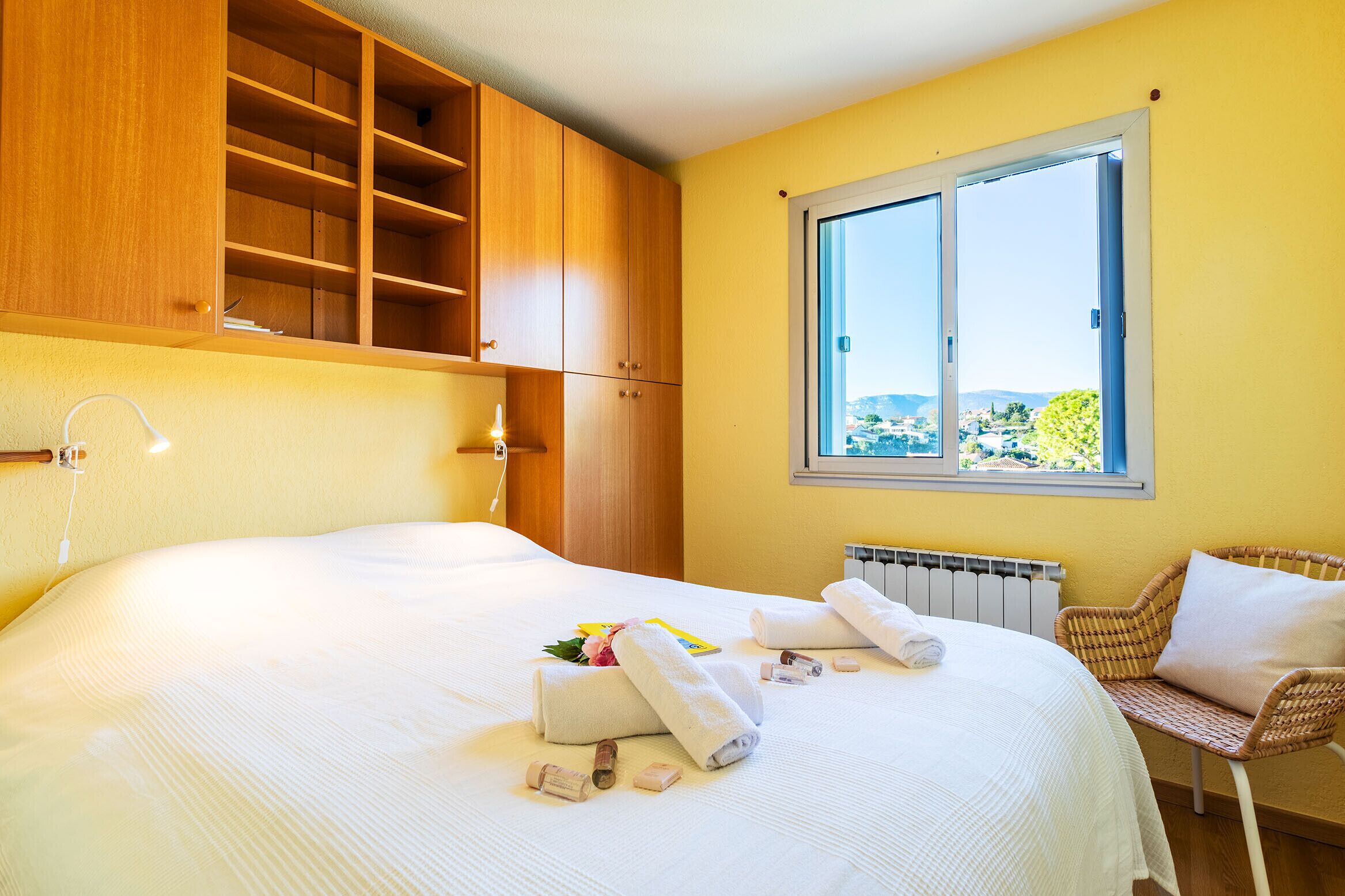 Ett hotellrum med en stor säng, en garderob i trä, ett fönster med utsikt och en fåtölj i rotting.