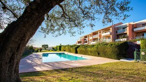 A modern apartment building with a swimming pool, surrounded by well-maintained hedges and a large tree. - LE JARDIN BLEU AP4388 By Riviera Holiday Homes (Niza)