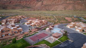 A residential area with modern houses, a swimming pool, tennis courts, and a desert landscape in the background.