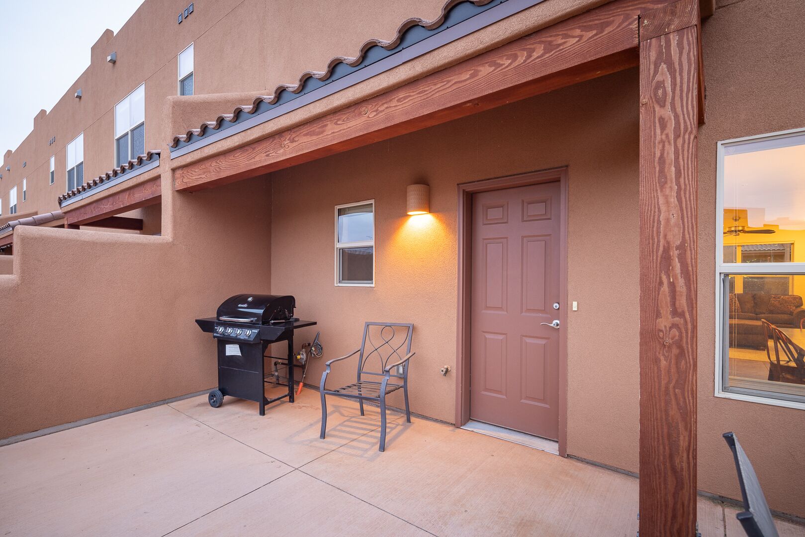A building exterior with a brown door, a barbecue grill, and a chair.