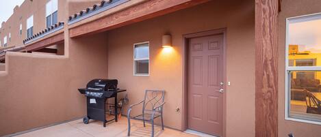 A building exterior with a brown door, a barbecue grill, and a chair.