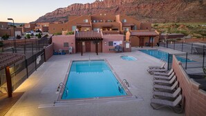 A hotel with a swimming pool, outdoor seating, and a mountainous backdrop.