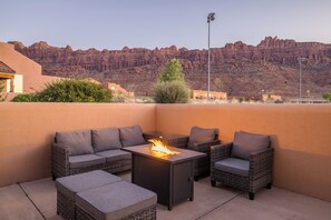 An outdoor patio with a fire feature, wicker furniture, and a view of red rock formations.