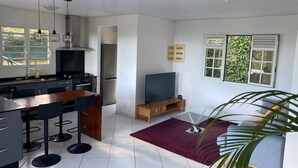 Een moderne keuken met een eethoek, een televisie en een groot raam met uitzicht op groen.