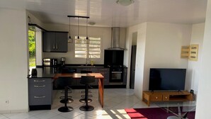 Een moderne keuken met een centraal eiland, een eethoek met barstoelen, een tv op een standaard en een rood vloerkleed.