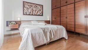 Ein Schlafzimmer mit einem großen Bett, einem Holzschrank und einem an der Wand hängenden abstrakten Gemälde.