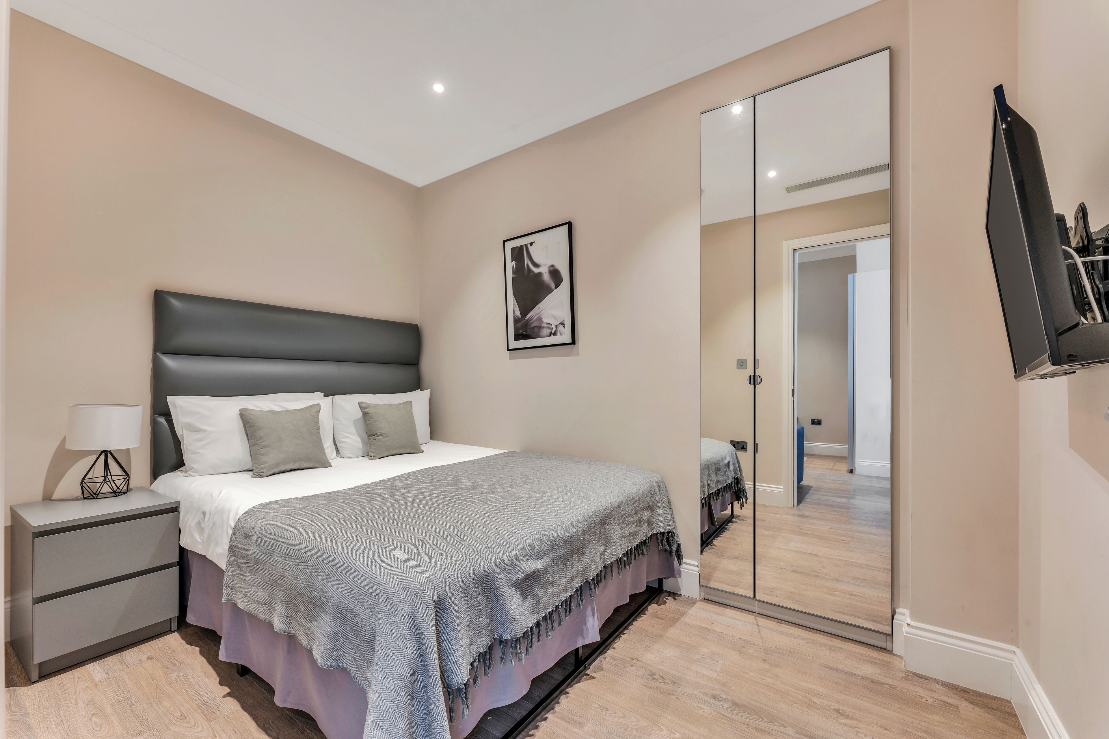 A bedroom with a bed, bedside table, lamp, and a mirror.