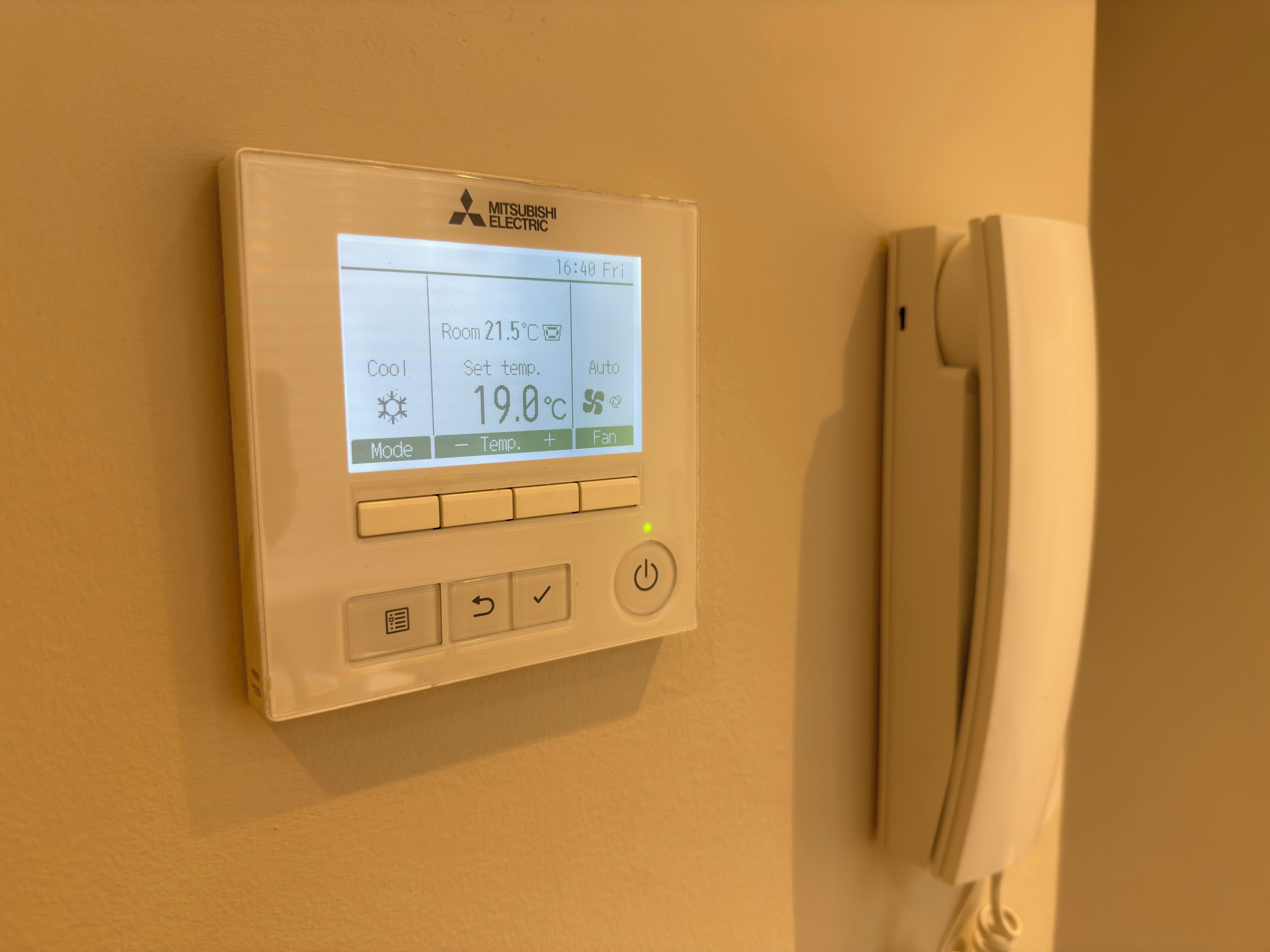A Mitsubishi Electric thermostat with a digital display, buttons, and a power switch.