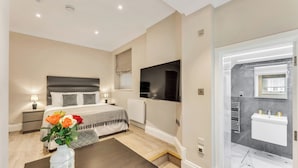A modern bedroom with a bed, bedside table, lamp, and a vase of flowers. - Cleveland Residences Chelsea (London)