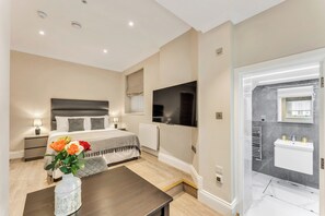 A modern bedroom with a bed, bedside table, lamp, and a vase of flowers. - Cleveland Residences Chelsea (London)