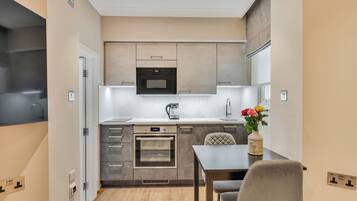 Una cocina compacta con electrodomésticos modernos, un comedor con mesa y sillas, y un pequeño jarrón con flores.