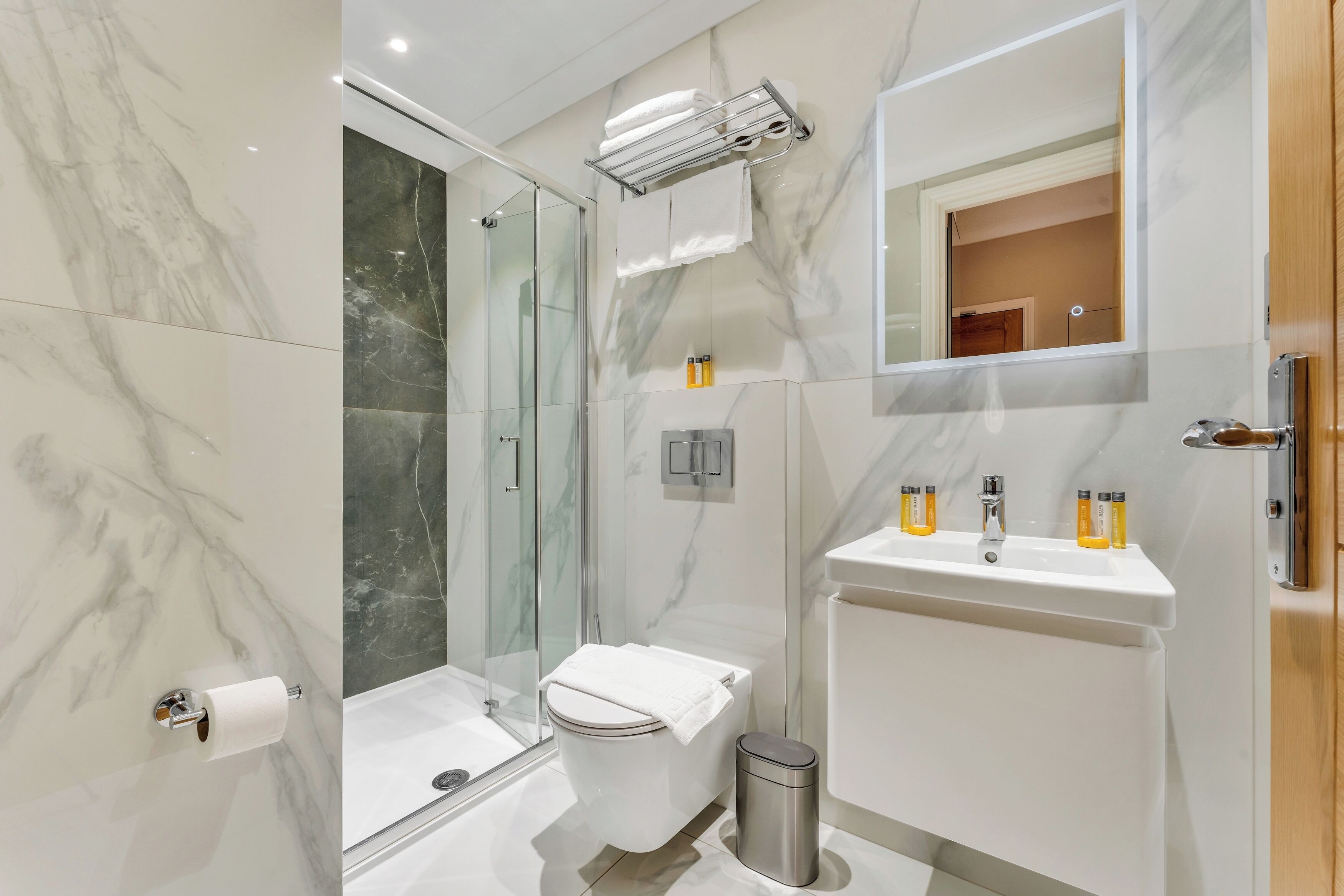 A modern bathroom with a glass shower enclosure, a toilet, a sink with toiletries, and a mirror.