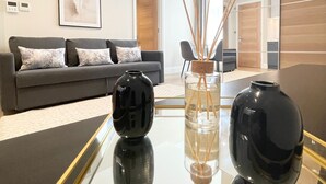 A modern living room with a glass-top coffee table, a grey sofa with patterned cushions, a framed artwork on the wall, and a wooden door in the background. - Cleveland Residences Chelsea (London)