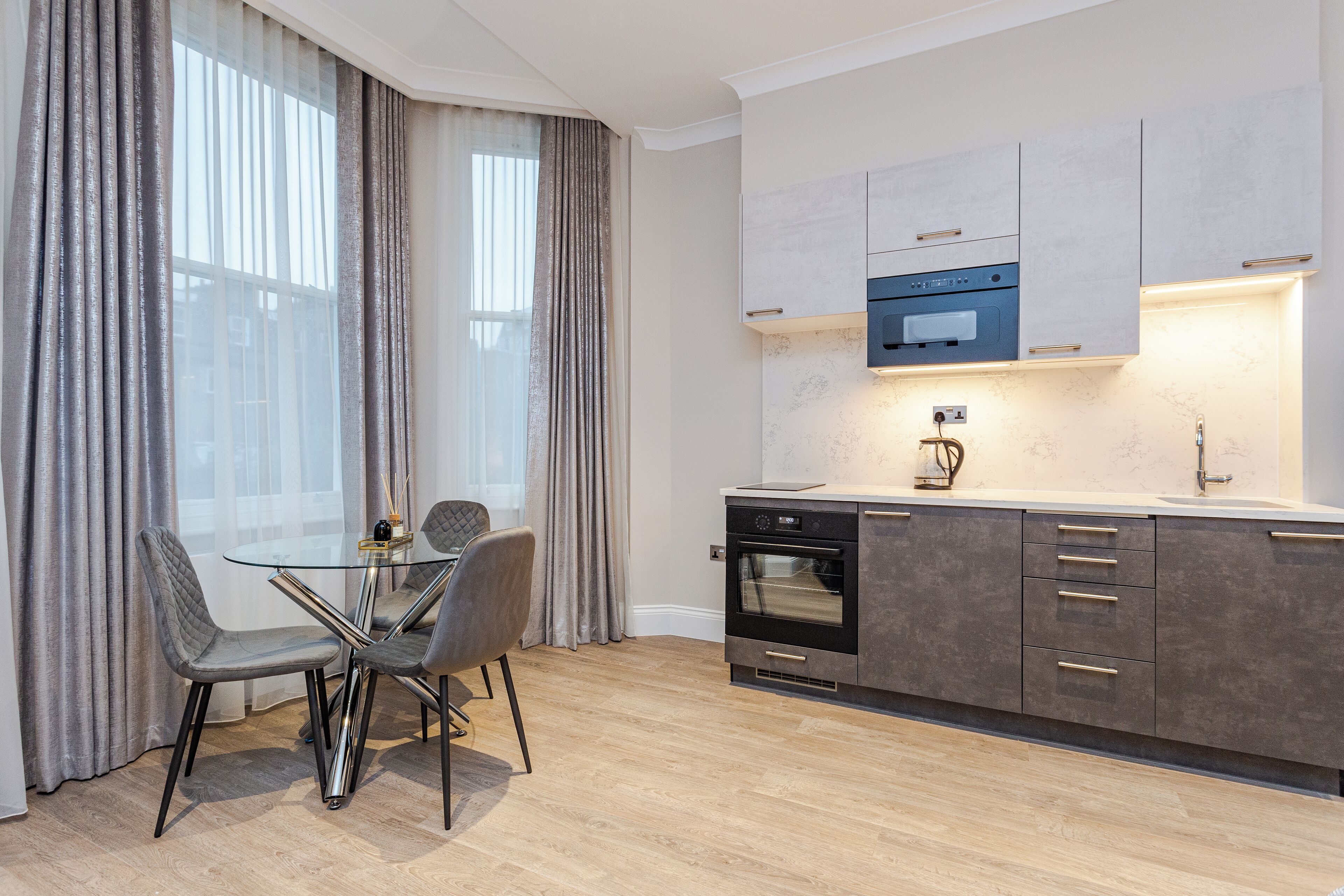 A modern kitchen with a built-in oven, a microwave, and a glass dining table with chairs.