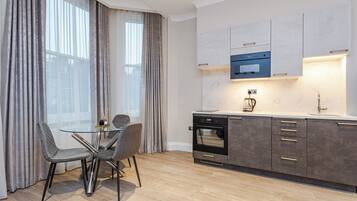 A modern kitchen with a built-in oven, a microwave, and a glass dining table with chairs.
