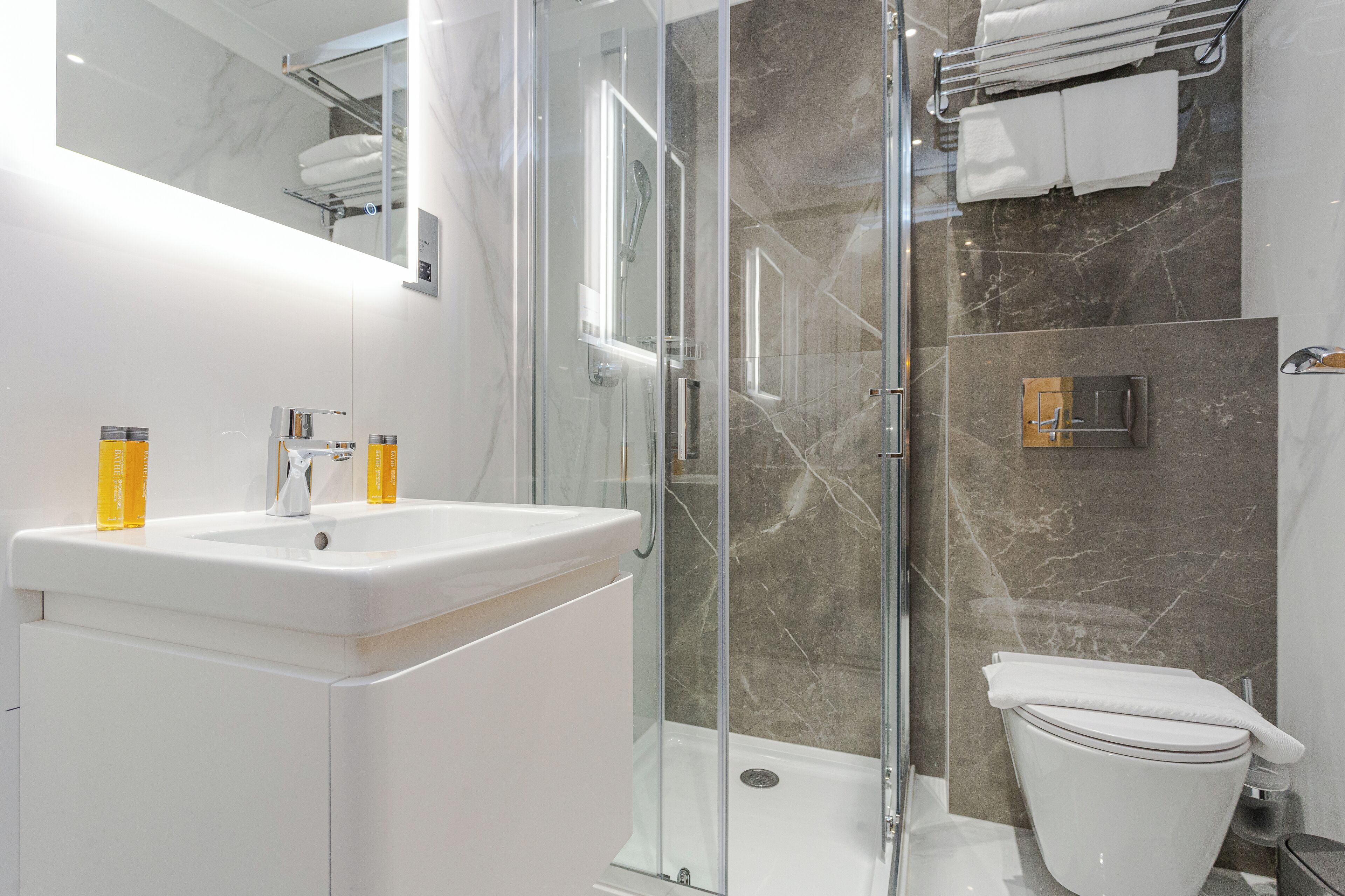 A modern bathroom with a glass-enclosed shower, a white sink with two yellow bottles, and a toilet.