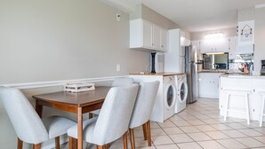 Een kleine keuken met een eethoek, inclusief een tafel met stoelen, een wasmachine en een koelkast.