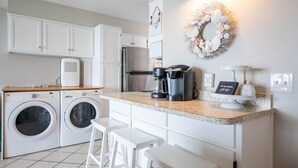 Een compacte keuken met een wasmachine, koffiezetapparaat en een klein eiland met krukken.